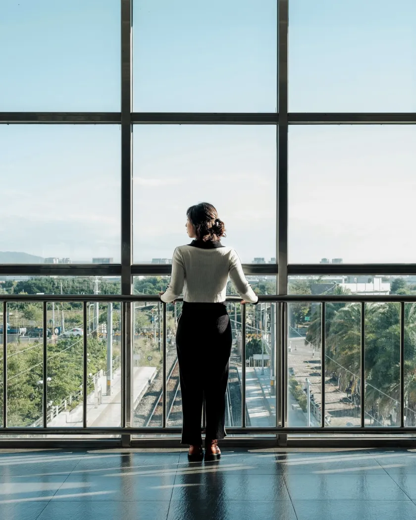 A woman standing before a glazed wall, looking out over the city with the viewer